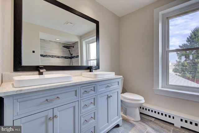 bathroom with a sink, a baseboard heating unit, double vanity, and a tile shower