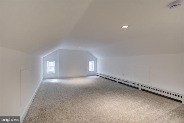 additional living space with a baseboard heating unit, carpet floors, a healthy amount of sunlight, and vaulted ceiling