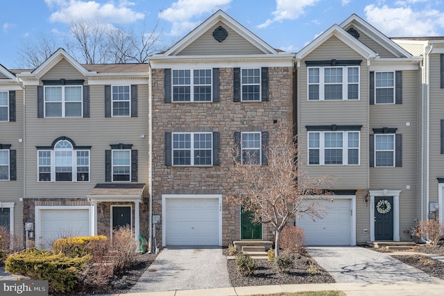 view of property featuring an attached garage, stone siding, and driveway