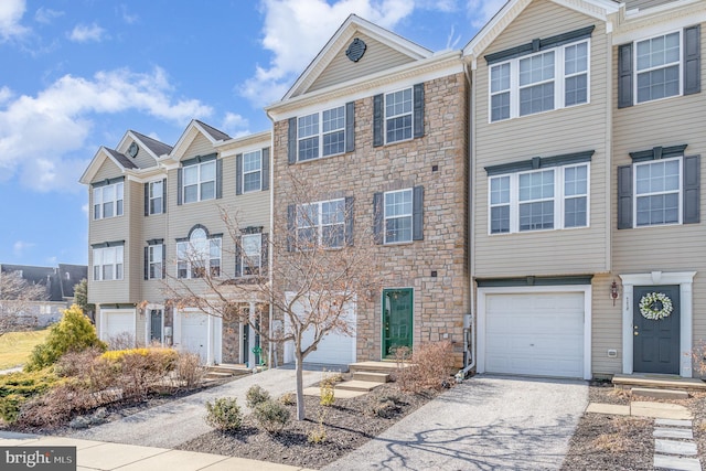 townhome / multi-family property with a garage, stone siding, and driveway