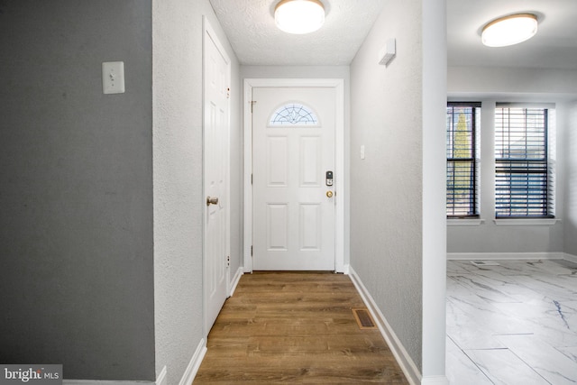 doorway featuring visible vents, a textured ceiling, baseboards, and a textured wall