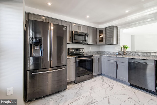 kitchen featuring a sink, light stone counters, appliances with stainless steel finishes, and gray cabinetry