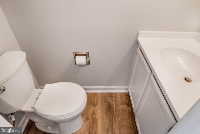 half bath with baseboards, toilet, wood finished floors, and vanity