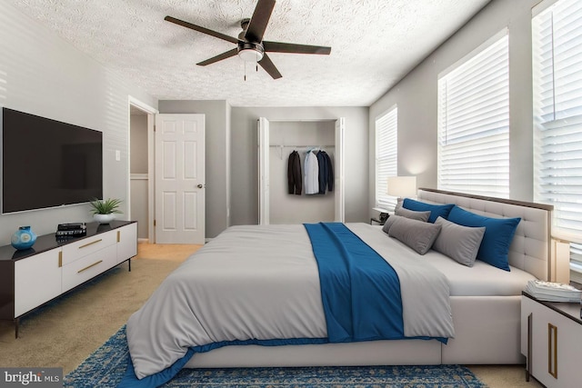 bedroom featuring a closet, light carpet, a textured ceiling, and a ceiling fan