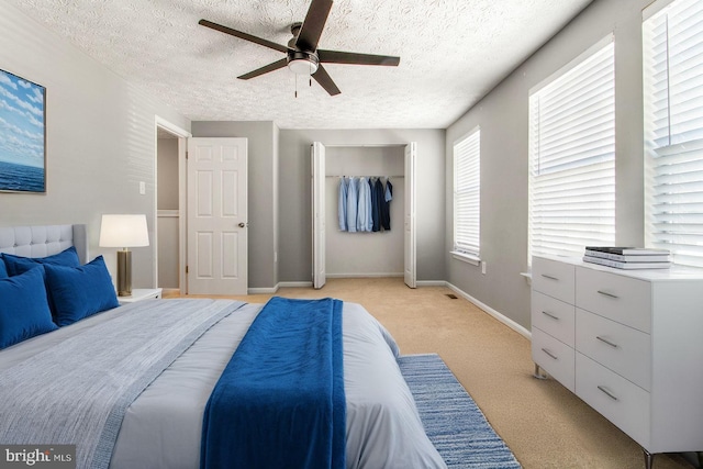 bedroom featuring a textured ceiling, a closet, baseboards, light colored carpet, and ceiling fan