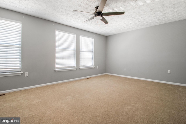 carpeted empty room featuring visible vents, a textured ceiling, baseboards, and a ceiling fan