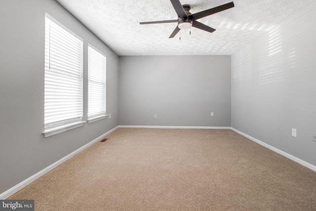 empty room with a textured ceiling, baseboards, visible vents, ceiling fan, and light carpet