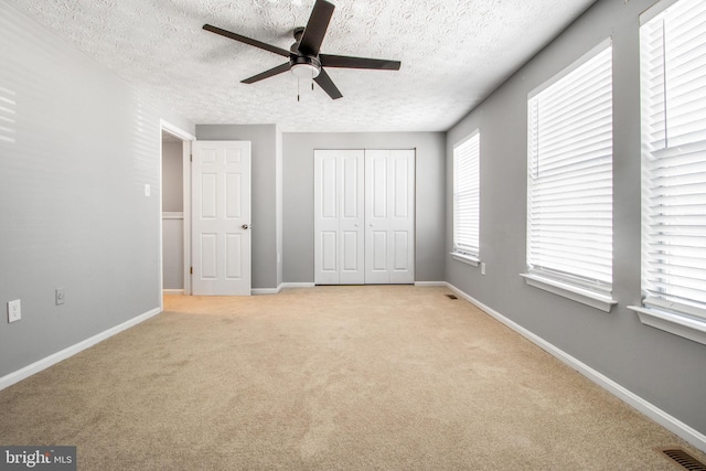 unfurnished bedroom with visible vents, light colored carpet, a textured ceiling, and baseboards