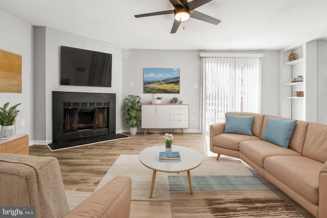 living area featuring a fireplace, baseboards, a ceiling fan, and wood finished floors