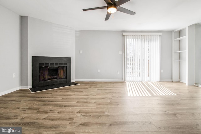 unfurnished living room featuring a ceiling fan, wood finished floors, a fireplace, and baseboards