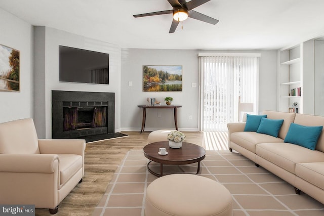 living room with a fireplace with flush hearth, baseboards, ceiling fan, and wood finished floors