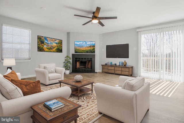 living room with wood finished floors, a fireplace, baseboards, and ceiling fan