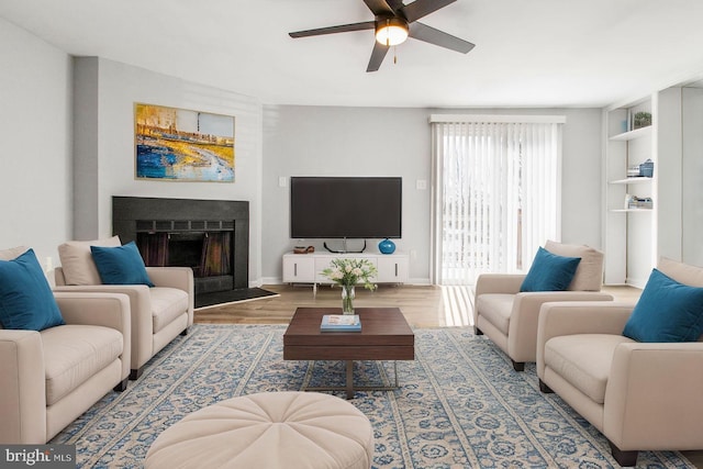 living area with a fireplace, baseboards, ceiling fan, and wood finished floors