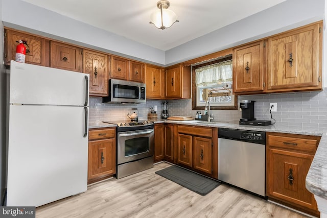 kitchen featuring brown cabinetry, a sink, stainless steel appliances, light wood-style floors, and tasteful backsplash