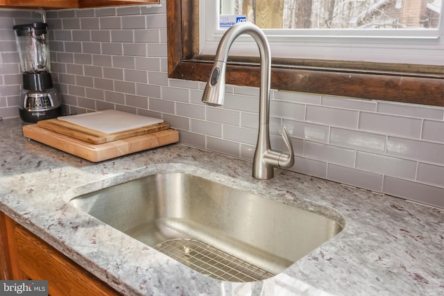 room details featuring light stone counters, brown cabinetry, tasteful backsplash, and a sink