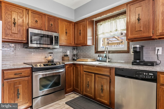 kitchen with brown cabinetry, backsplash, appliances with stainless steel finishes, and a sink