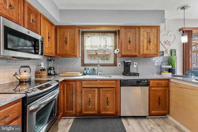 kitchen featuring decorative backsplash, light wood-style flooring, appliances with stainless steel finishes, brown cabinetry, and a sink