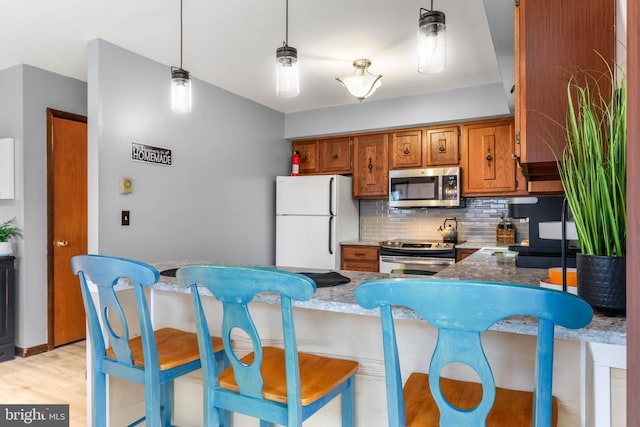 kitchen with a breakfast bar area, brown cabinetry, a peninsula, stainless steel appliances, and tasteful backsplash