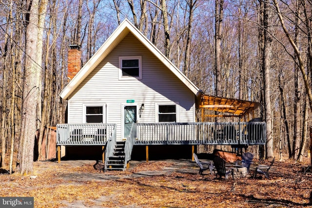 back of property featuring a wooded view, a fire pit, a chimney, and a wooden deck