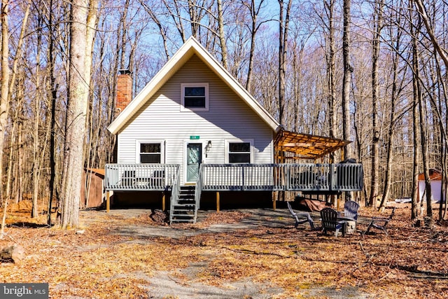 rear view of house featuring a chimney, a deck, and a view of trees