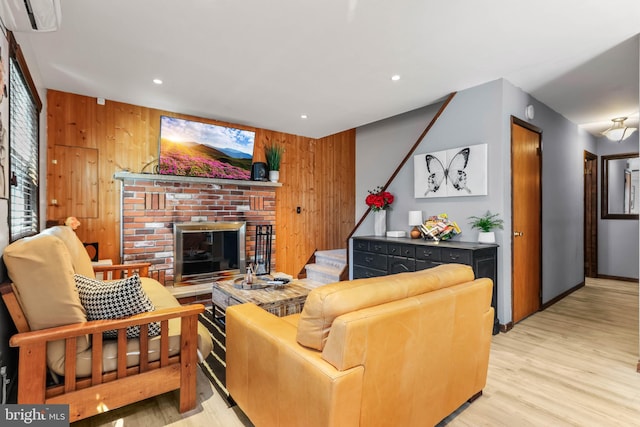 living room with light wood finished floors, wooden walls, a brick fireplace, stairway, and recessed lighting