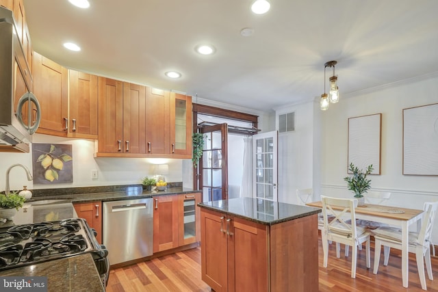 kitchen with visible vents, glass insert cabinets, crown molding, light wood-style flooring, and appliances with stainless steel finishes