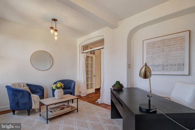 living area featuring beamed ceiling, wood finished floors, arched walkways, and baseboards