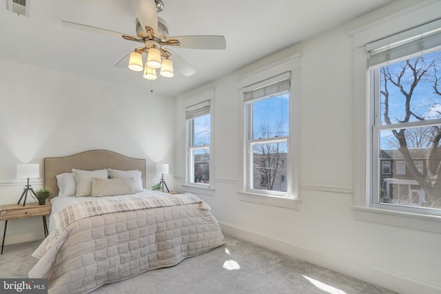 carpeted bedroom with multiple windows, baseboards, visible vents, and ceiling fan