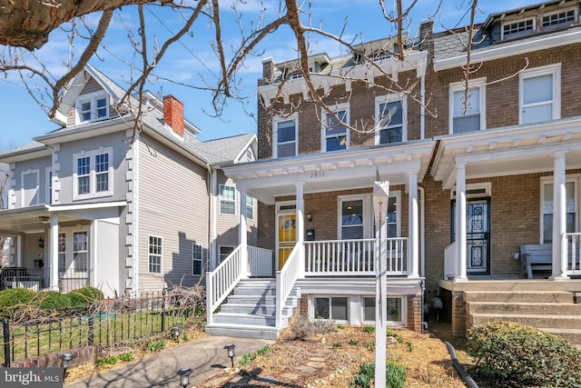 multi unit property featuring brick siding, a porch, and fence