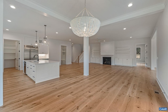 kitchen featuring a center island with sink, light wood finished floors, a sink, white cabinetry, and a large fireplace