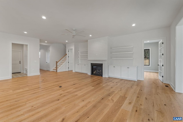 unfurnished living room with baseboards, light wood-style flooring, recessed lighting, a fireplace, and stairs