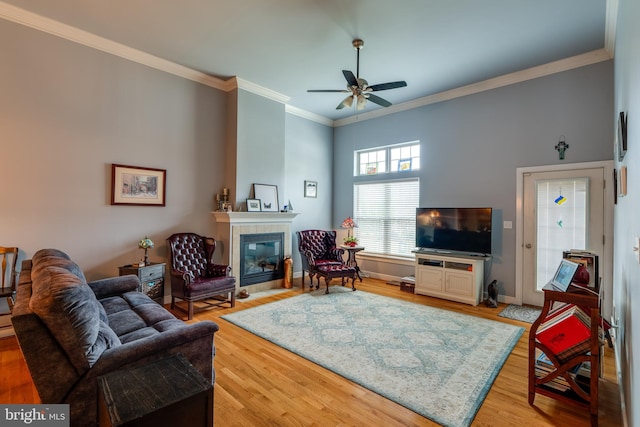 living room featuring baseboards, ornamental molding, a tile fireplace, ceiling fan, and light wood-style floors