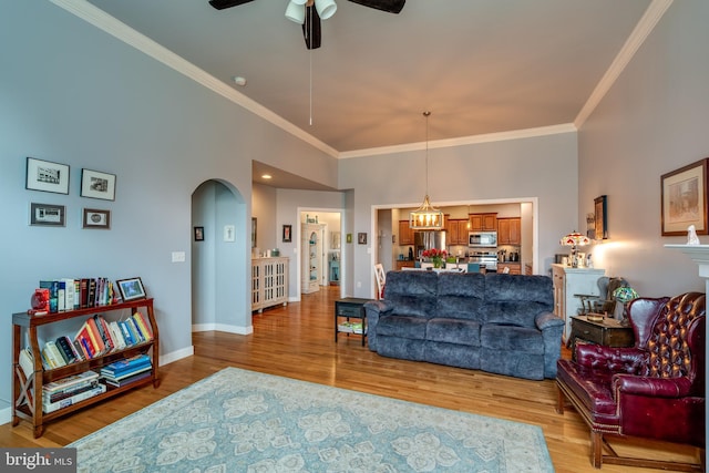 living area featuring a high ceiling, arched walkways, ornamental molding, ceiling fan with notable chandelier, and light wood-type flooring