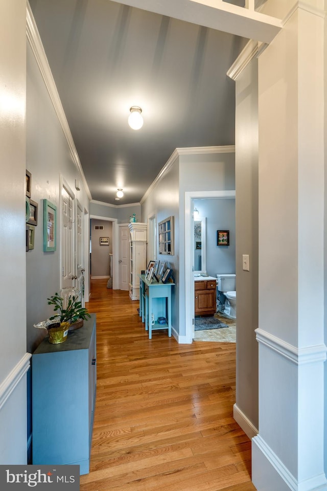 hallway featuring baseboards, light wood-style flooring, and ornamental molding