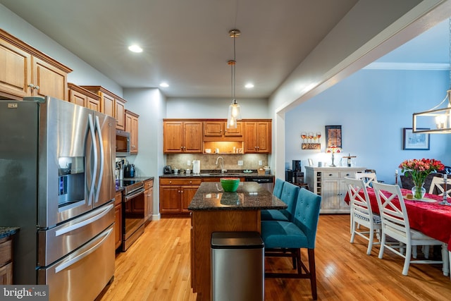 kitchen featuring a breakfast bar area, light wood finished floors, a kitchen island, decorative backsplash, and appliances with stainless steel finishes