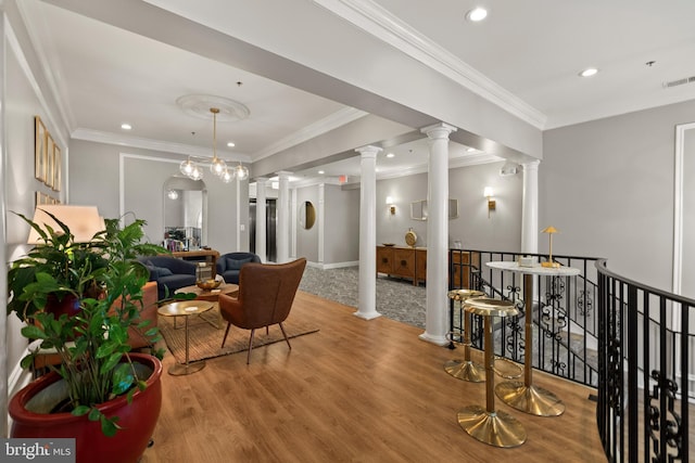 interior space featuring visible vents, an upstairs landing, ornamental molding, wood finished floors, and ornate columns