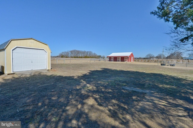 view of yard with a rural view, a detached garage, an outbuilding, and fence