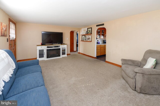 carpeted living room with arched walkways, a fireplace, and baseboards