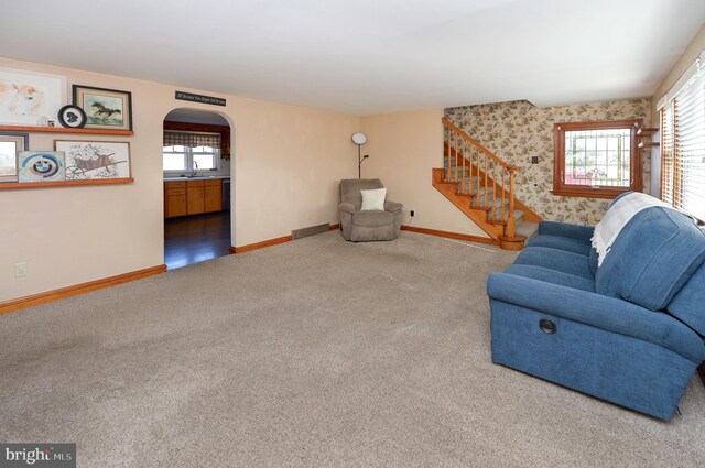 carpeted living area with stairs, arched walkways, baseboards, and a sink