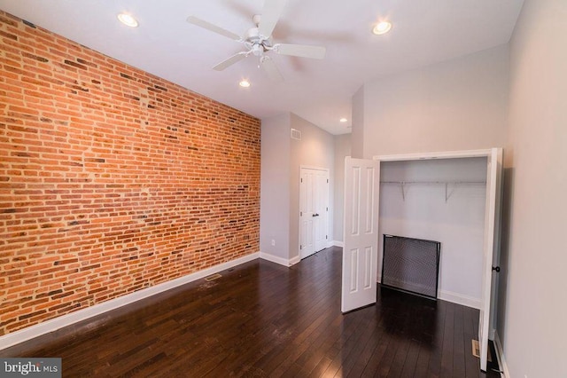 unfurnished living room with hardwood / wood-style floors, baseboards, brick wall, and ceiling fan