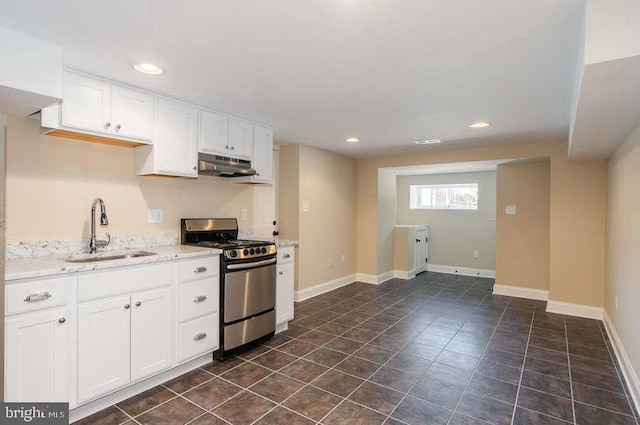 kitchen featuring stainless steel gas range oven, baseboards, under cabinet range hood, white cabinetry, and a sink