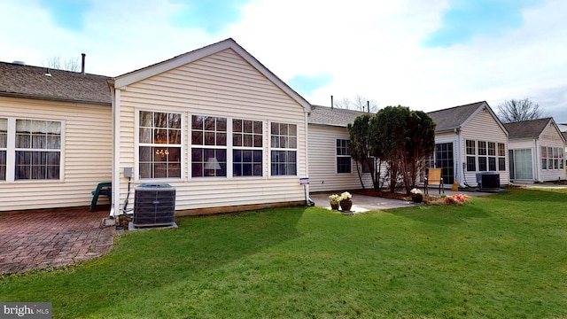 back of property featuring cooling unit, a patio area, a lawn, and roof with shingles