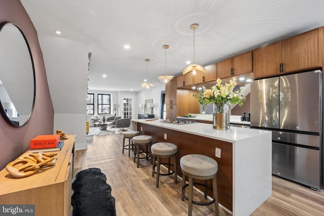 kitchen with light wood-type flooring, stainless steel appliances, a kitchen bar, and light countertops