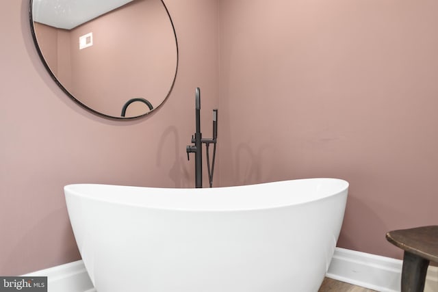 bathroom with visible vents, a freestanding bath, baseboards, and wood finished floors