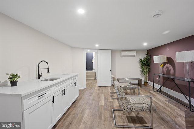 kitchen with baseboards, a wall mounted AC, a sink, white cabinetry, and light wood-type flooring