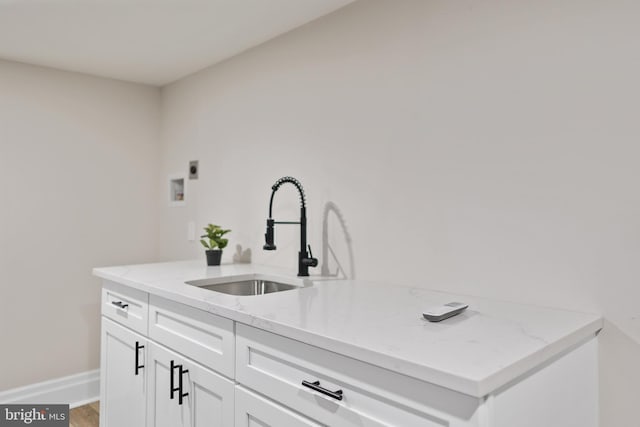 kitchen with light wood-type flooring, a sink, light stone counters, white cabinets, and baseboards