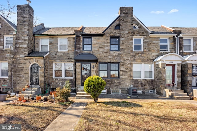 townhome / multi-family property with a front lawn, cooling unit, stone siding, and a chimney