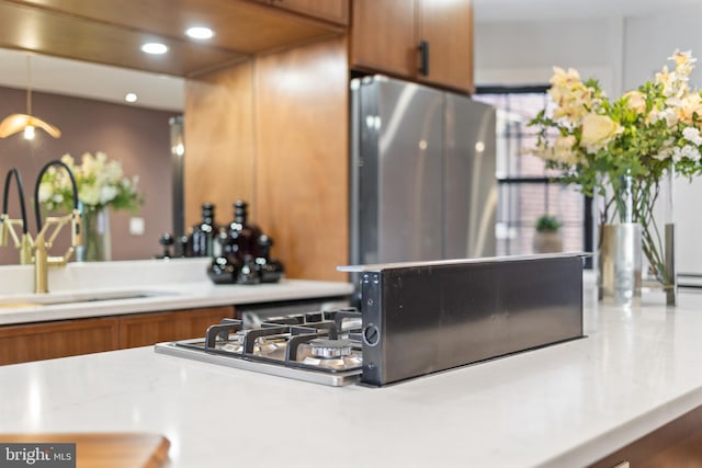 kitchen featuring stainless steel gas cooktop, light countertops, recessed lighting, brown cabinetry, and a sink