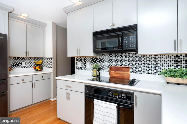 kitchen featuring light countertops, decorative backsplash, light wood-style flooring, white cabinets, and black appliances