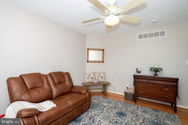 living room featuring ceiling fan, visible vents, baseboards, and wood finished floors